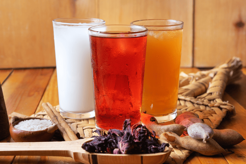 Jarras o vasos con aguas frescas mexicanas de colores vivos (Jamaica, Horchata, Tamarindo).