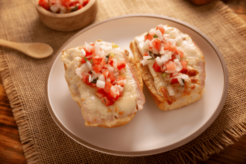 Molletes abiertos en bolillo, con frijoles refritos, queso derretido y pico de gallo encima.